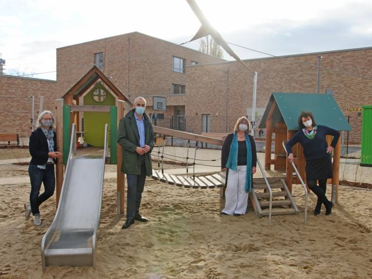 Vier Personen auf dem Hof einer Kita. Sie tragen einen Mund-Nasen-Schutz. 