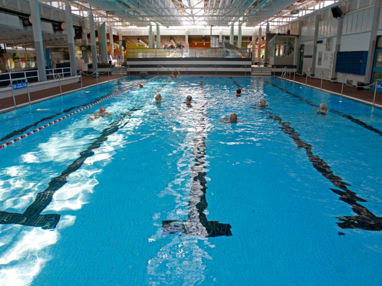 Eine Schwimmhalle mit einigen Menschen im Wasser. 