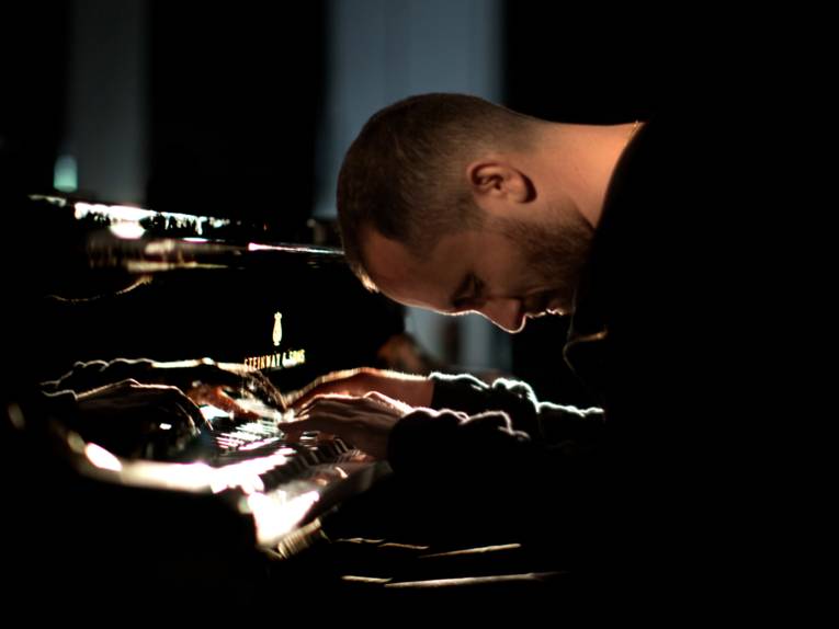 Ein Mann spielt Klavier, lehnt sich dabei mit dem Oberkörper nach vorn