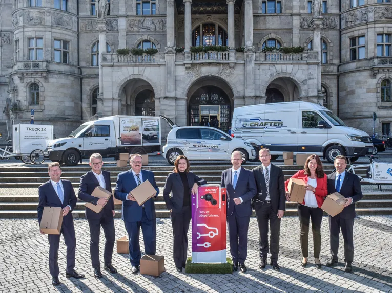 Die Repräsentanten der Partner zum Start der Initiative Urbane Logistik Hannover vor dem neuen Rathaus mit verschiedenen Fahrzeugen im Hintergrund.
