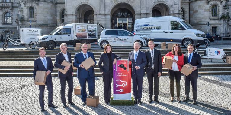Die Repräsentanten der Partner zum Start der Initiative Urbane Logistik Hannover vor dem neuen Rathaus mit verschiedenen Fahrzeugen im Hintergrund.
