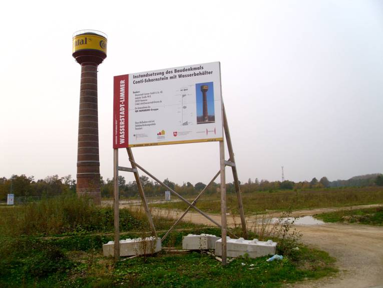 Conti-Schornstein mit Wasserbehälter, im Bildvordergrund ein Bauschild 