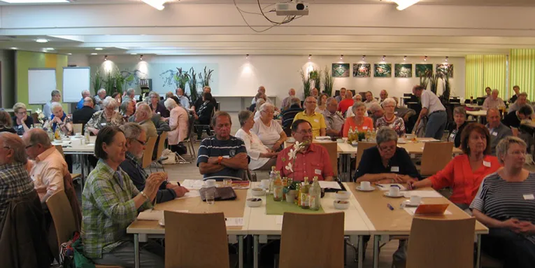 Blick in einen gut besuchten Saal, an dem Delegierte in Gruppen an Tischen sitzen