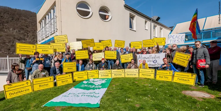 Gruppenfoto: Mit symbolischen Ortsschildern mit der Aufschrift "Atomwaffenverbot" zeigen Bürgermeisterinnen und Bürgermeister, Abgeordnete und Friedensaktivisten ihre Haltung für ein weltweites Atomwaffenverbot.