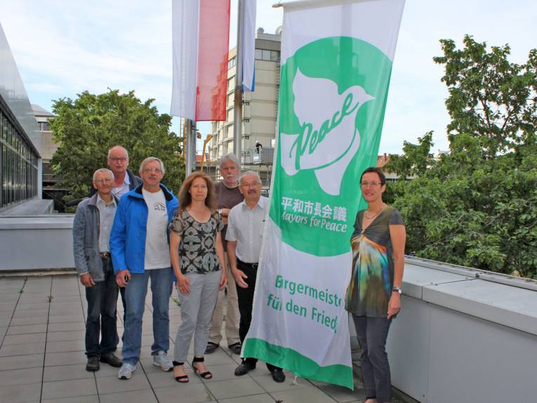 Bürgermeisterin von Erlangen und sechs weitere Personen neben der Flagge "Bürgermeister für den Frieden"