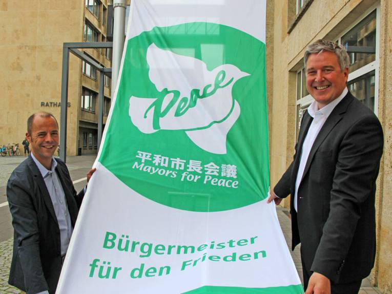 Bürgermeister und Integrationsbeauftragter der Stadt Gütersloh zeigen die Flagge der "Bürgermeister für den Frieden"