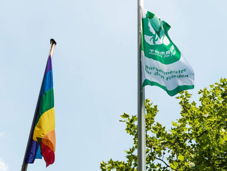Die Bürgermeister-für-den-Frieden-Flagge neben der Regenbogen-Fahne.