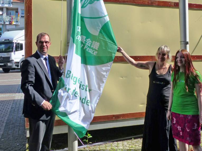 Mühlackers Oberbürgermeister Frank Schneider mit zwei weiblichen Mitgliedern der Friedensgruppe "Friedenszeit" beim Hissen der "Mayors for Peace"-Flagge