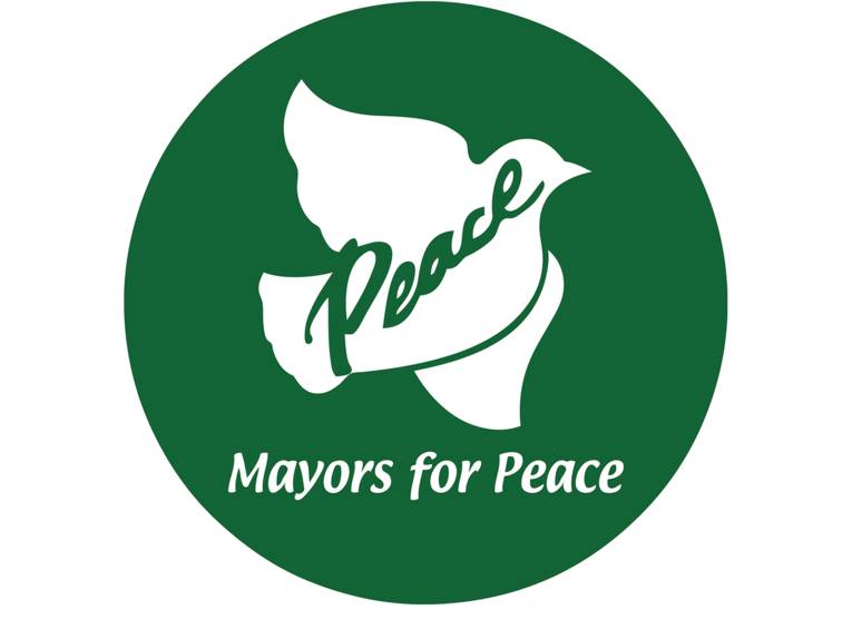 Das Logo zeigt eine weiße Taube auf grünem Grund mit den Worten "Mayors for Peace".