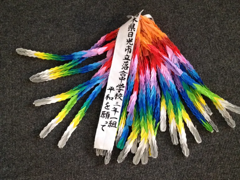 Bunte Papierkraniche mit einem Band mit japanischen Schriftzeichen