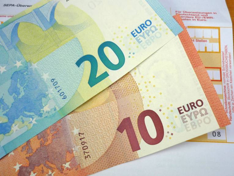 Ein Zwanzig-Euro-Schein und ein Zehn-Euro-Schein auf einem Überweisungsträger