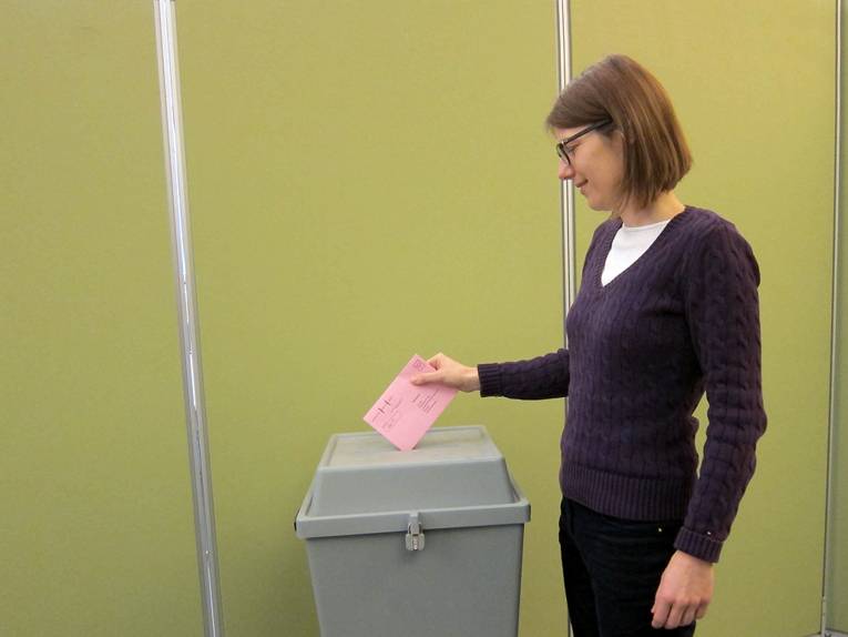 Eine Frau wirft einen Briefumschlag in eine Wahlurne (nachgestellte Szene)