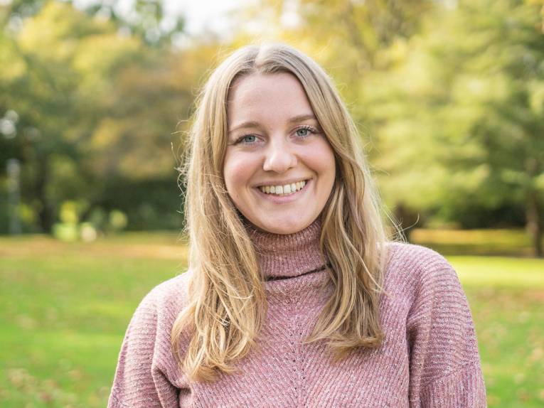 Porträt einer Frau, im Hintergrund Bäume und Sträucher