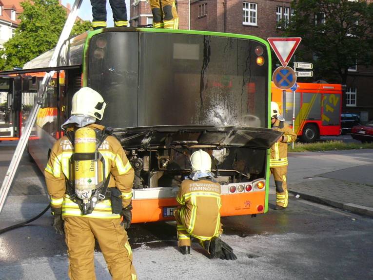 Einsatzkräfte der Feuerwehr kontrollieren den Motorraum des Linienbusses nach einem gezieltem Löschangriff.