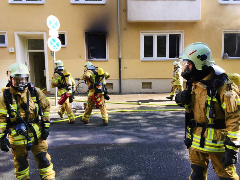 Mehrere Atemschutzgeräteträger der Feuerwehr Hannover vor der betroffenen Wohnung.
Im Hintergrund Fenster mit Rauchentwicklung.