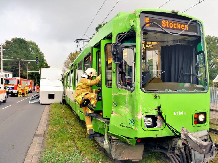 Im Vordergrund eine Einsatzkraft der Feuerwehr Hannover, die in die beschädigte Stadtbahn steigt. Im Hintergrund das beschädigte Führerhaus des LKWs sowie weitere Einsatzkräfte und Einsatzwagen.