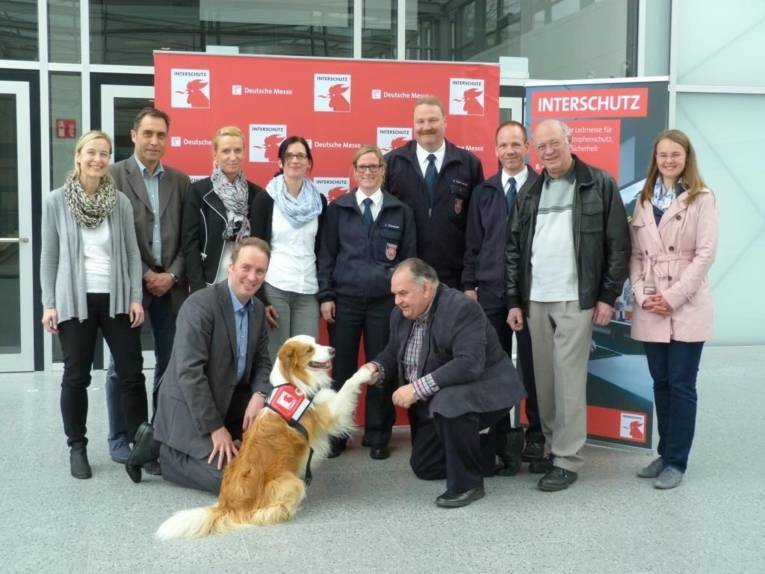Die weltgrößte Messe für Brand- und Katastrophenschutz, Rettung und Sicherheit, die INTERSCHUTZ in Hannover, hat jetzt ein eigenes Maskottchen: Rettungshund Timmy. Messe-Projektleiter Heinold und das Team von Deutscher Messe AG, vfdb und Feuerwehr Hannover begrüßen Timmy.