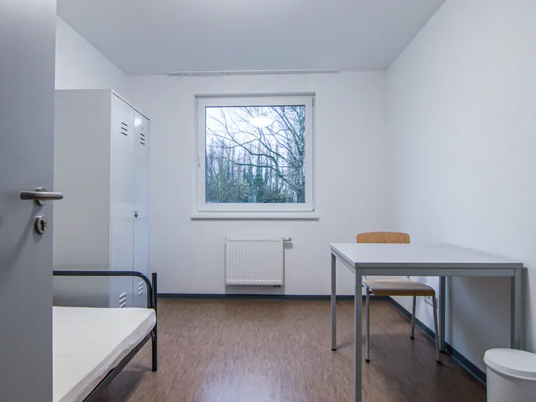 Ein Raum mit einem Bett, einem Stuhl, einem Tisch und einem Schrank