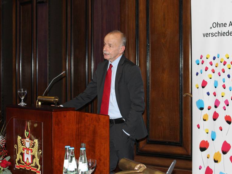 Ein Mann steht im Hodlersaal des Neuen Rathauses hinter einem Pult und spricht.