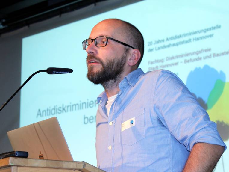 Ein Mann steht hinter einem Pult und spricht in ein Mikrofon.