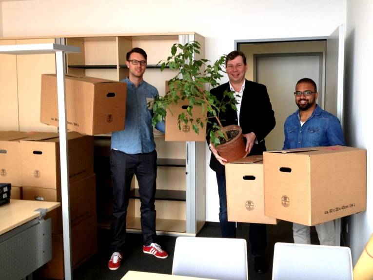 Drei Männer stehen in einem Büro und halten Umzugskartons in den Händen