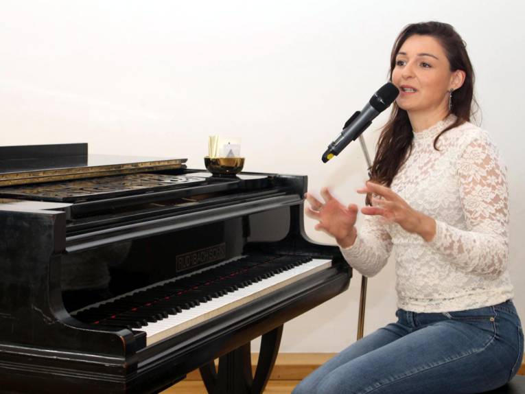 Eine Frau sitzt auf einem Klavierstuhl vor einem Flügel und sing in ein Mikrofon.