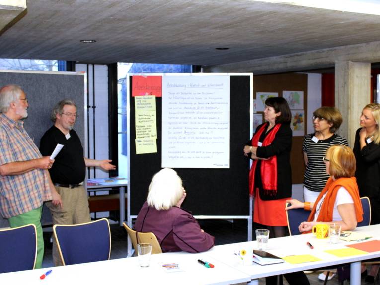 Fünf Personen - zwei Männer und drei Frauen stehen liks und rechts von einem Flipchart, an dem verschieden große Zettel befestigt sind. Die handschriftliche Überschrift des großen Zettels lautet: "Hannover steht bei Sprachförderung auf der Leitung.