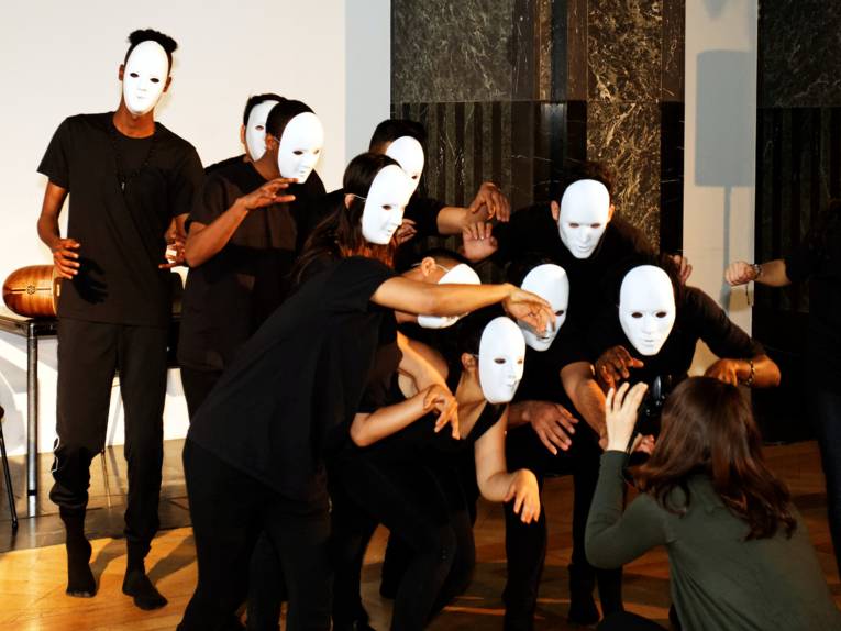 Etwa 10 schwarz gekleidete Jugendliche tragen weiße Masken und posieren vor einer Fotografin.