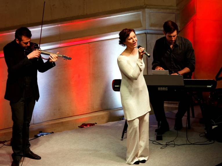 Die Sängerin Anna Nova steht mit Mikrofon in der Hand während ein Geiger und ein Keyboarder sie begleiten