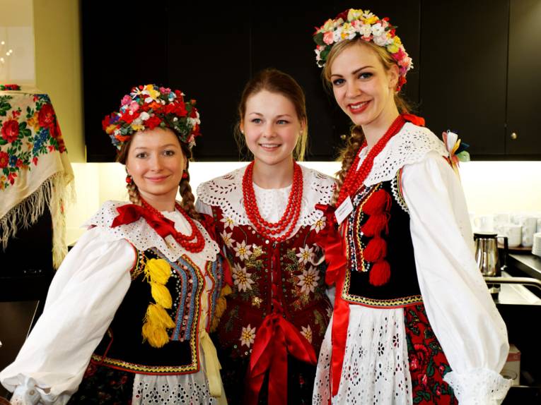 Gruppenbild mit drei Frauen in bunter Tracht, links steht Katarzyna Dec-Merkle, eine Mitarbeiterin im Fachbereich Bildung und Qualifizierung der LHH