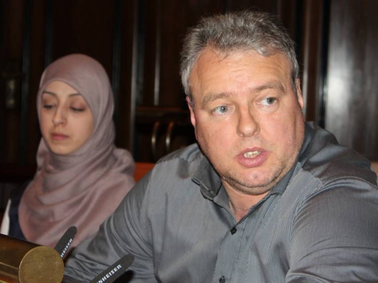 Ein Mann sitzt im Hodlersaal hinter einem Pult und spricht. Links daneben ist eine Frau erkennbar.