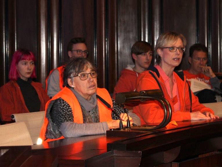 Sechs mit Schwimm- und Warnwesten bekleidete Personen sitzen im Hodlersaal neben- und hintereinander. Eine Frau in der vorderen Reihe spricht in ein Mikrofon.