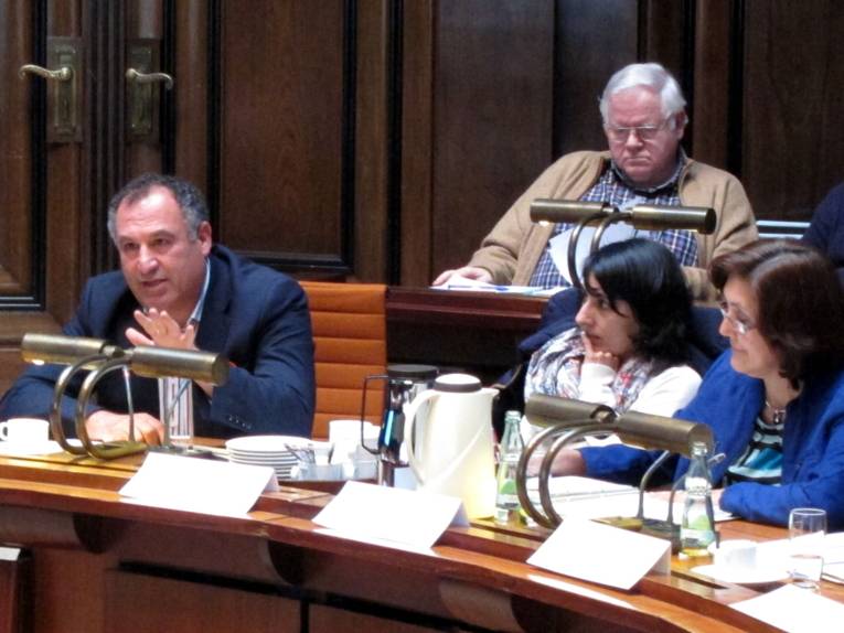 Drei Personen sitzen hinter Pulten. Oben ist noch ein Zuhörer erkannbar, der jedoch nicht zum Ausschuss gehört. Der Mann links im Bild spricht.