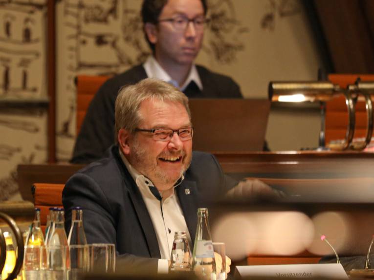 Ein Mann sitzt im Hodlersaal hinter einem Pult und lacht.