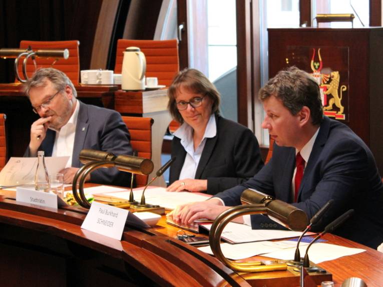 Drei Personen sitzen im Hodlersaal hinter Pulten. 