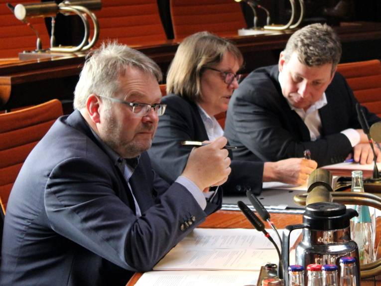 Drei Personen sitzen im Holdersaal nebeneinander hinter Pulten.