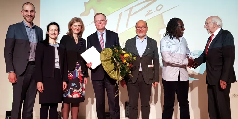 Sieben Personen - zwei Frauen und fünf Männer - stehen nebeneinander auf der Bühne des Europasaals und blicken nach vorn.