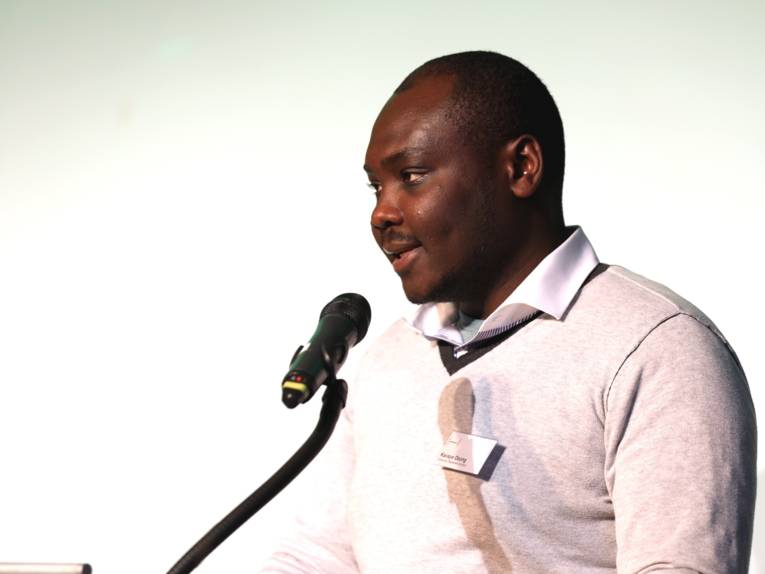 Ein Mann steht im Europasaal des Hauses der Jugend an einem Redner*innnenpult und spricht