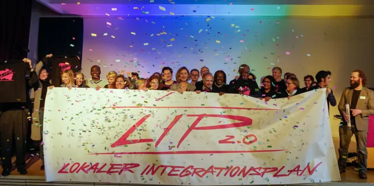Etwa 20 Personen stehen hinter einem Banner, auf dem "LIP 2.0" steht, während Konfetti hinabregnet