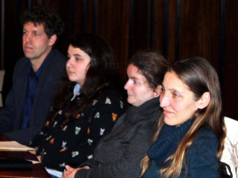 Vier Personen - drei Frauen und ein Mann - sitzen im Hodlersaal hinter Pulten und blicken nach vorne