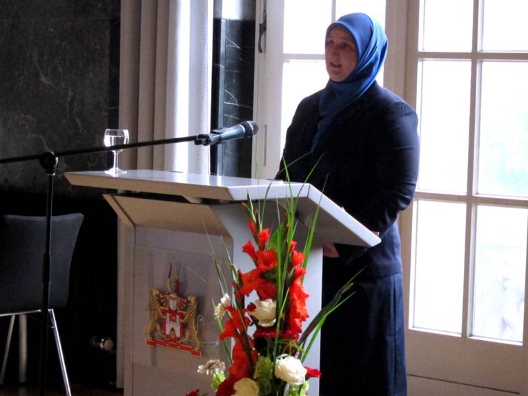 Eine Frau steht hinter einem Rednerpult und spricht in ein Mikrofon.