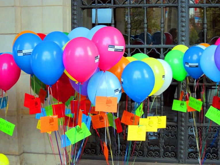 Unter den lilanen, roten, gelben, weißen, grünen, hell- und dunkelblauen Luftballons ( insgesamt etwa 30) sind Zierbänder, an denen die Postkarten befestigt sind.