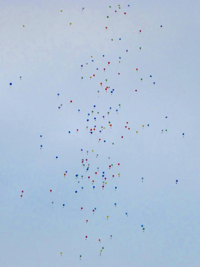 Etwa 200 Ballons schweben im hellblauen Himmel.