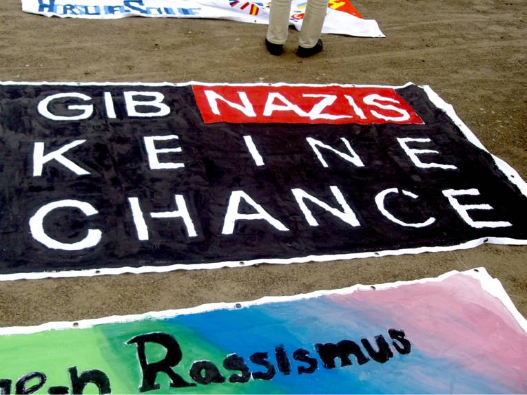 Ein großes Transparent liegt am Boden auf dem mit Plakafarben gemalt ist: "Gib' Nazis keine Chance!"