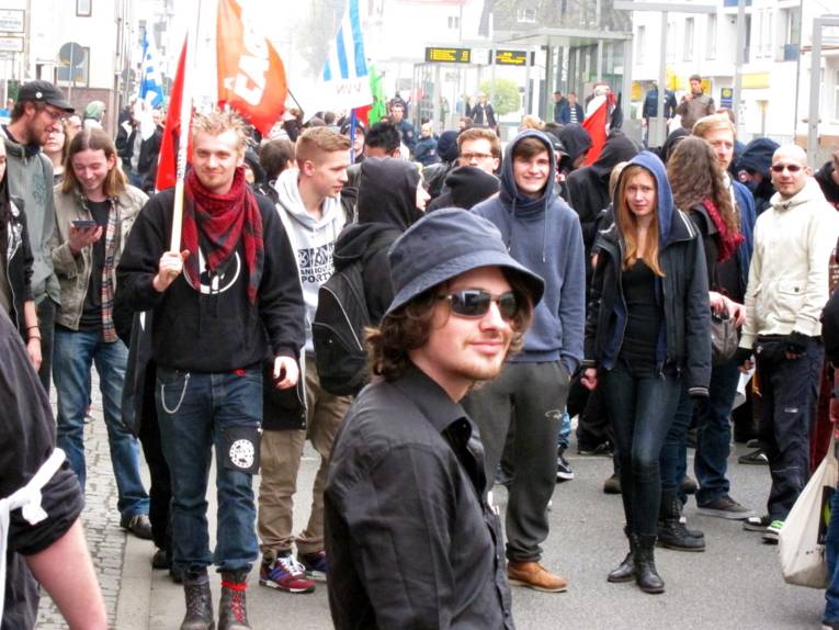 Etwa 50 Jugendliche stehen in kleinen und größeren Gruppen zusammen und unterhalten sich. Im Vordergrund und im Hintergrund sind etwa 5 rote und blau-weiße Fahnen erkennbar.