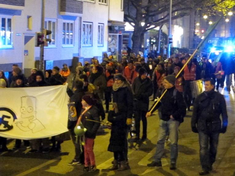 Etwa 80 Personen laufen eine Straße entlang. Die vorderen Teilnehmer haten ein Transparent mit einem durchgestrichenen Hakenkreuz vor sich, weiter hinten sind Fahnen zu erkennen.