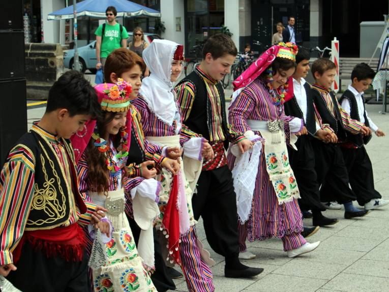 Neun Kinder in traditioneller Folklore-Kleidung stehen in einer Reihe und fassen sich an den Händen an.