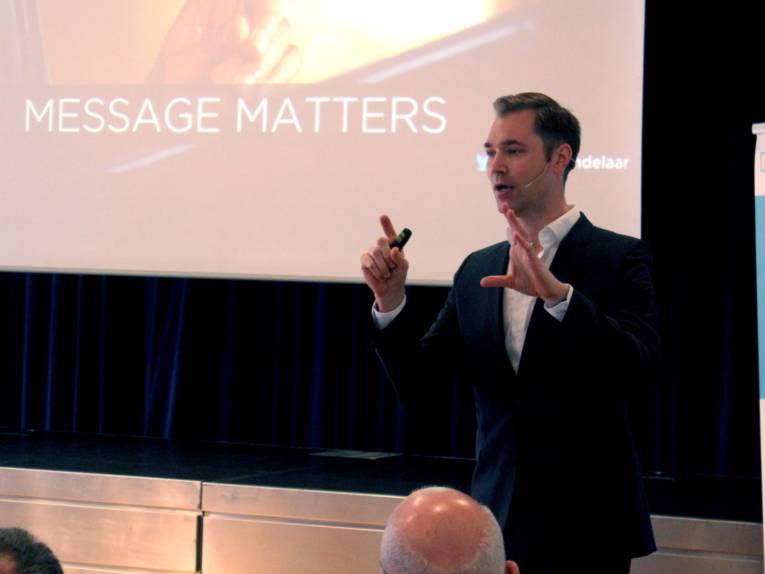 Ein Mann gestikuliert beim Sprechen. Hinter ihm ist ein Teil seiner Power-Point-Präsentation erkennbar, auf der „Message matters“ steht.