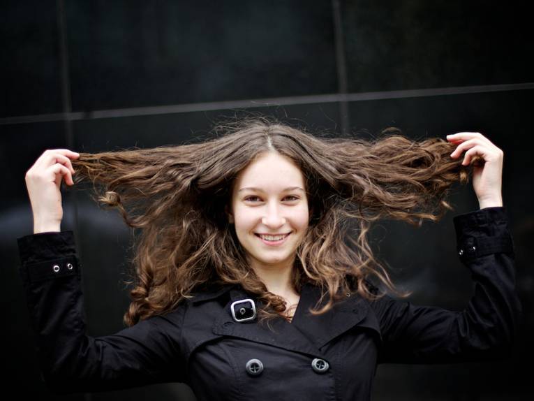Ein Mädchen zieht ihre Haare locker zu den Seiten auseinander