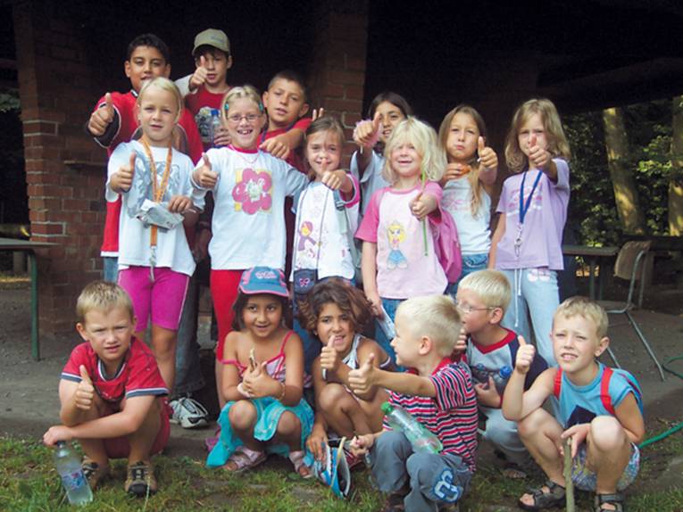 Eine Gruppe Kinder hält vor einem Familienzentrum die Daumen hoch